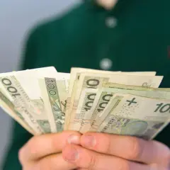 Dłonie trzymające plik banknotów 100 zł. Zastanawiasz się, ile wynosi renta rodzinna dla dziecka?