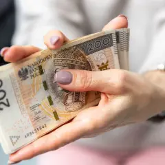 Dłonie trzymają plik banknotów 200 zł. Czekanie na decyzję o przyznaniu emerytury może być długie, ale pieniądze są ważne.