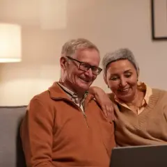 Uśmiechnięta para seniorów na kanapie przegląda poradnik: jak chorobowe wpływa na wysokość emerytury.