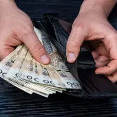 Dłonie trzymają portfel z polskimi banknotami. Czy wdowa może przejąć emeryturę po mężu? Pieniądze w portfelu.
