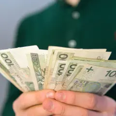 Dłonie trzymające plik banknotów 100 zł. Pytanie: ile wynosi renta rodzinna po zmarłym mężu?