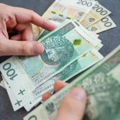 Dłonie liczą polskie banknoty 100 zł i 200 zł. Czy to wystarczy, by pokryć ile wynosi najniższa renta rodzinna?