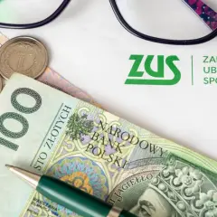 ZUS i pieniądze, by dowiedzieć się, ile wynosi renta po zmarłym ojcu. Okulary i długopis sugerują analizę dokumentów.