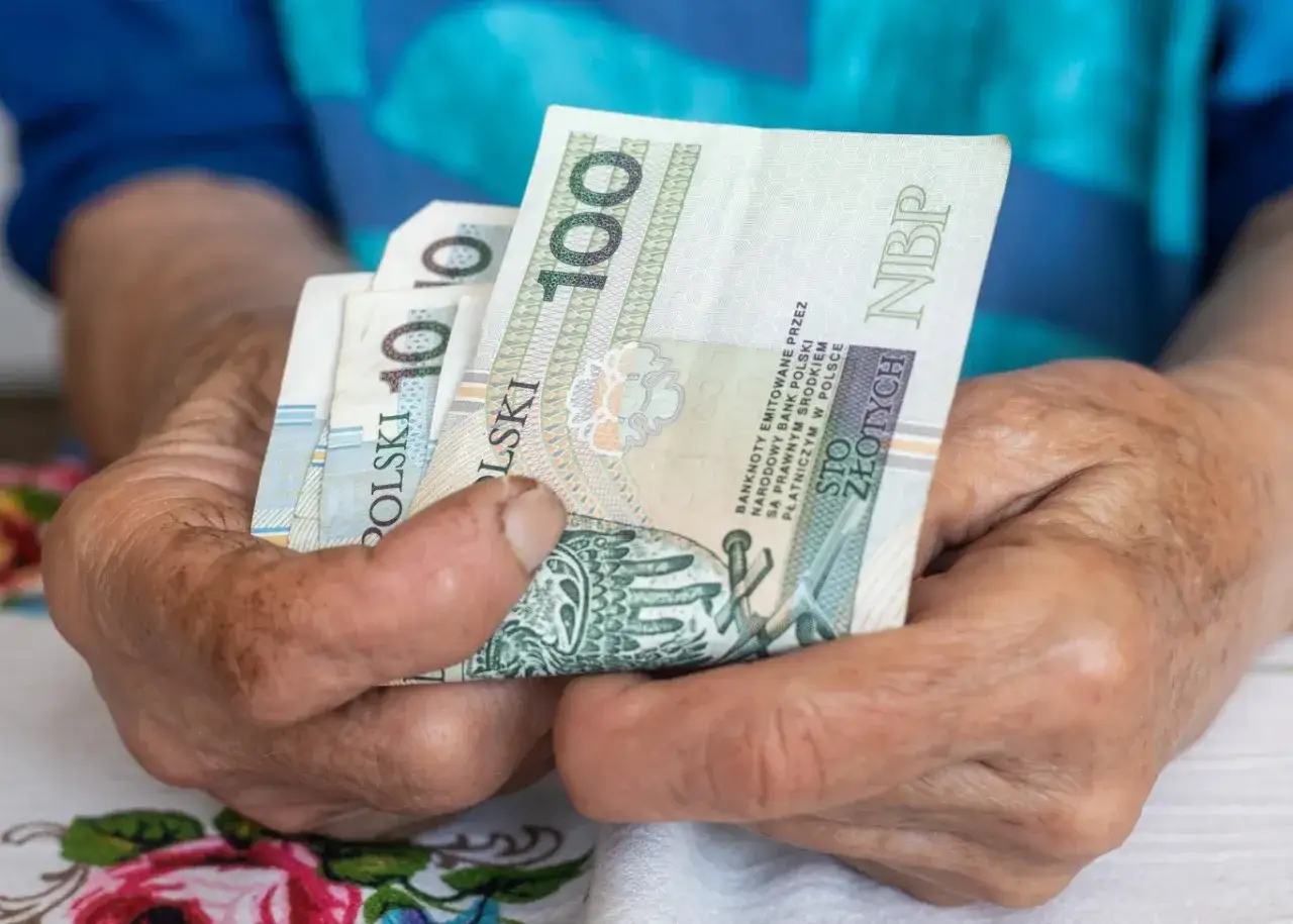 Dłonie trzymające banknoty 100 zł. Pytanie brzmi, ile można zarabiać na emeryturze, gdy liczy się każdy grosz.