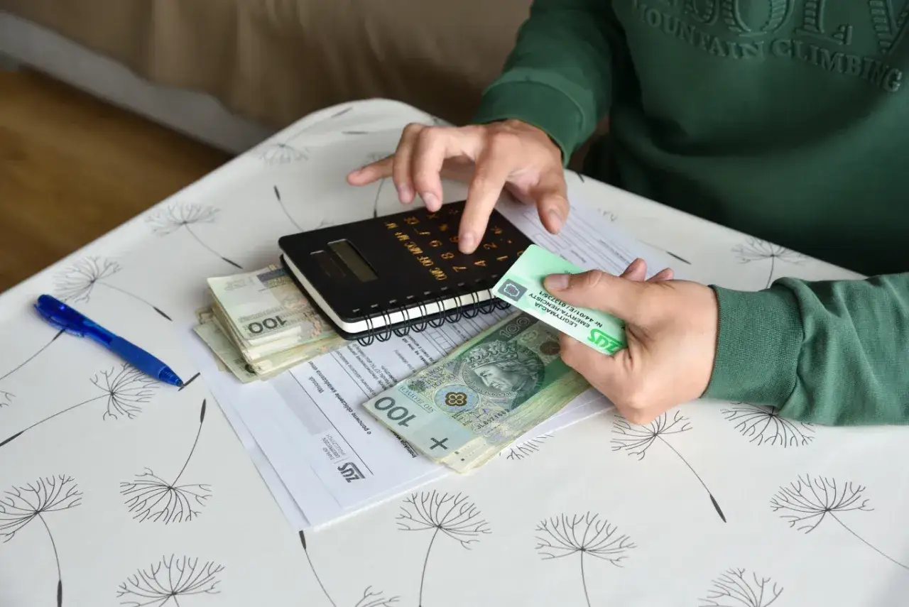 Osoba liczy pieniądze i legitymację ZUS, zastanawiając się, czy renta zależy od zarobków.