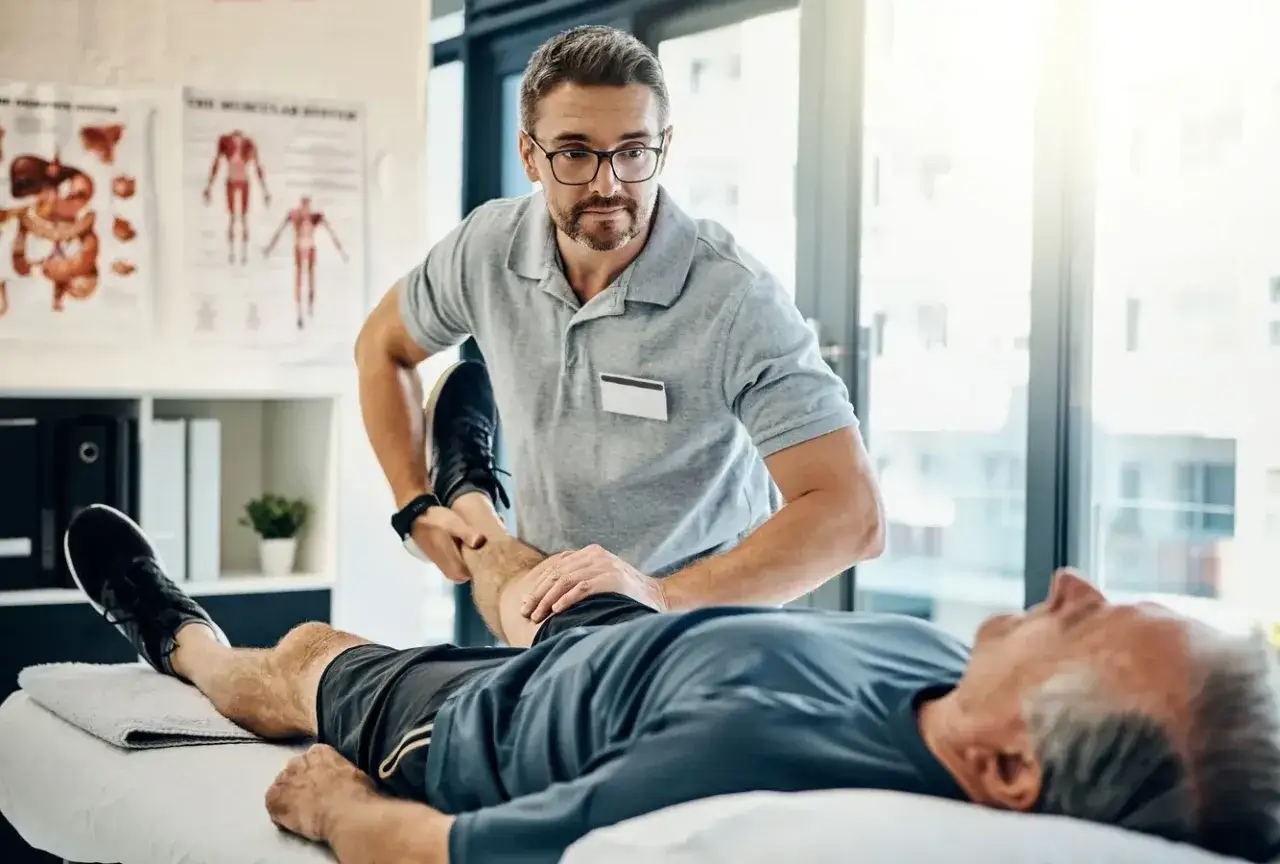 Fizjoterapeuta pomaga pacjentowi w ćwiczeniach. Długość rehabilitacji zależy od wielu czynników, w tym od stanu zdrowia i postępów.