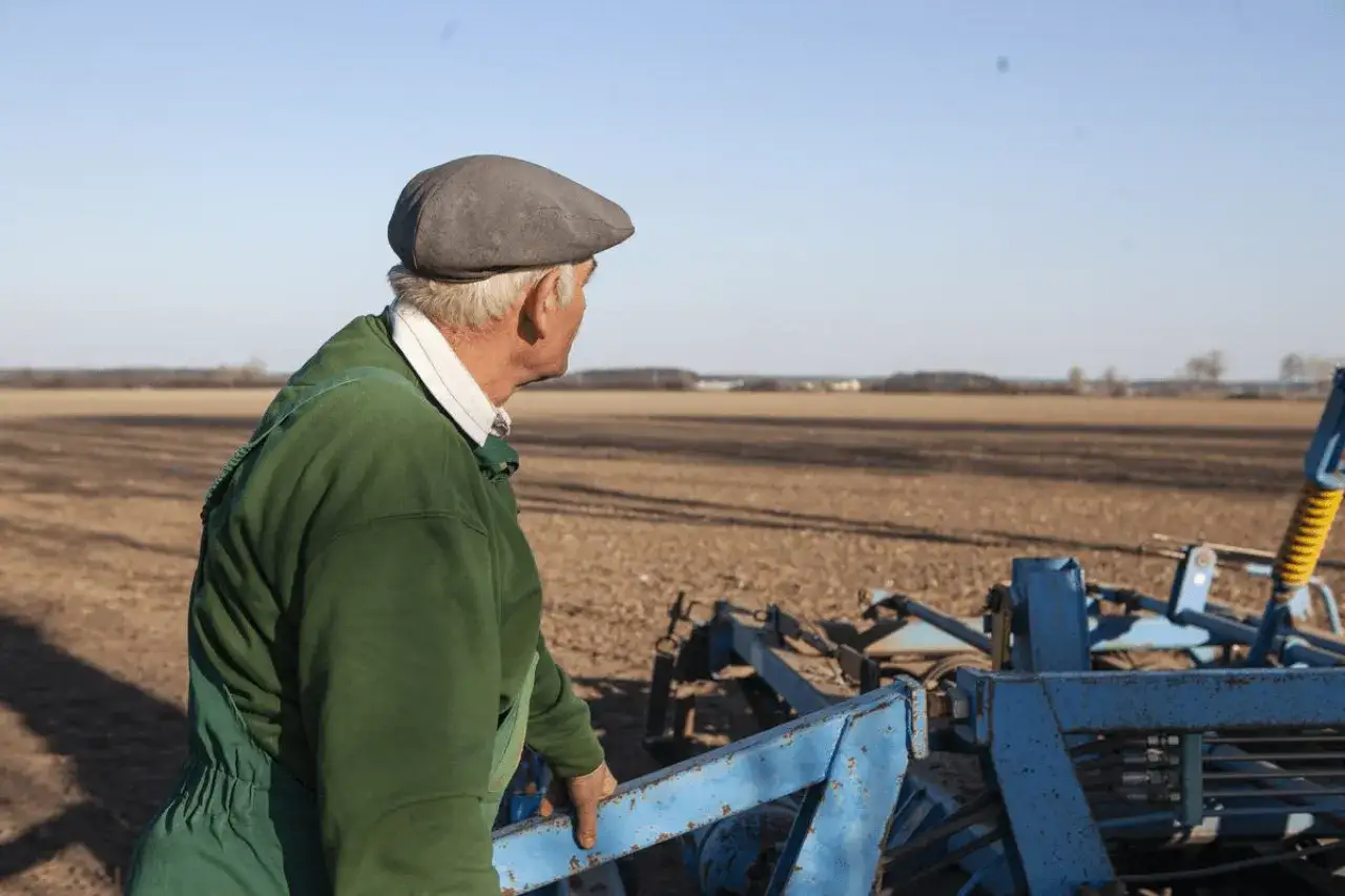 Rolnik w zielonym ogrodniczkach i czapce patrzy na pole. Zastanawia się, kiedy rolnik może iść na emeryturę.